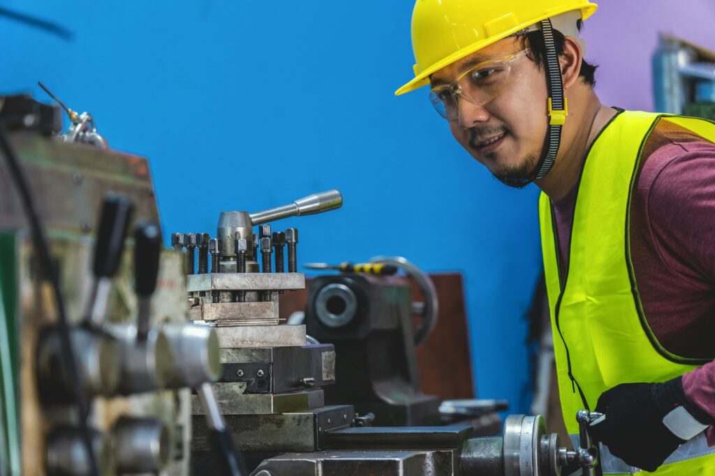 Asian machinist in safety suit operating the professional lathes in metalworking factory,